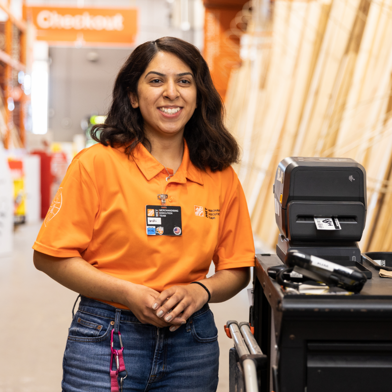 Hispanic female wearing orange polo shirt stands next to merchandising equipment.
