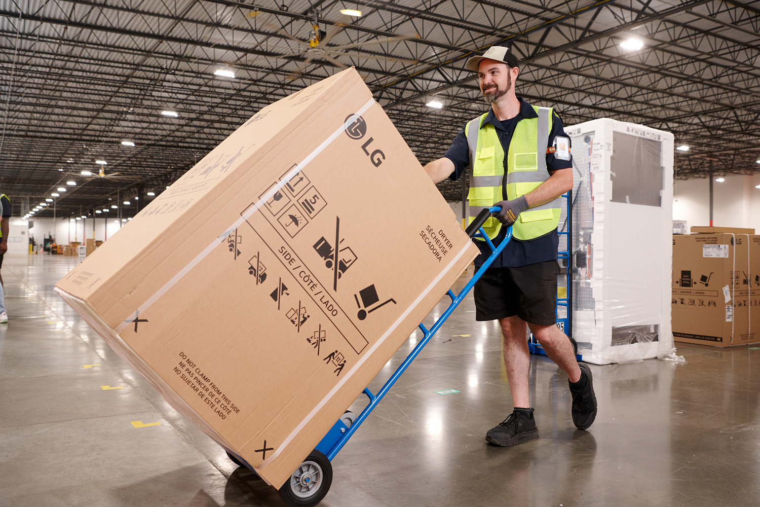 An associate moving a large boxed appliance on a hand truck in a warehouse