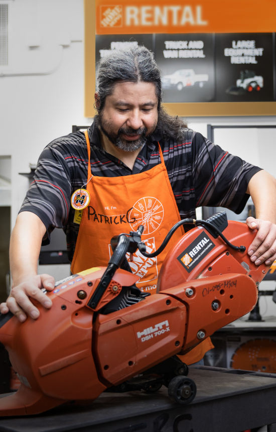 Man in an orange Home Depot apron, inspecting a large power tool